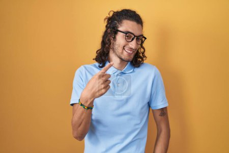 Foto de Joven hombre hispano de pie sobre fondo amarillo haciendo señas ven aquí gesto con la mano invitando a la bienvenida feliz y sonriente - Imagen libre de derechos