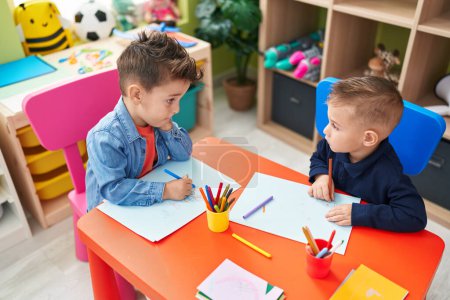 Téléchargez les photos : Adorables garçons enfants d'âge préscolaire assis sur la table dessin sur papier à la maternelle - en image libre de droit