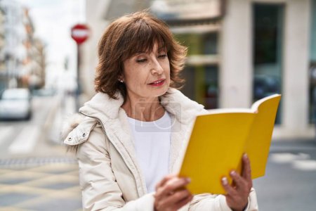 Téléchargez les photos : Femme d'âge moyen lecture livre à la rue - en image libre de droit