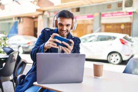Téléchargez les photos : Young hispanic man playing video game sitting on table at coffee shop terrace - en image libre de droit