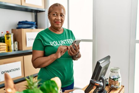 Foto de Mujer afroamericana mayor vistiendo uniforme voluntario usando teléfono inteligente en el centro de caridad - Imagen libre de derechos
