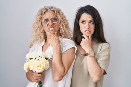 Photo for Mother and daughter holding bouquet of white flowers thinking worried about a question, concerned and nervous with hand on chin - Royalty Free Image