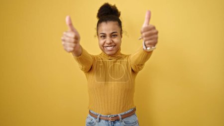 Photo for Young african american woman smiling with thumbs up over isolated yellow background - Royalty Free Image