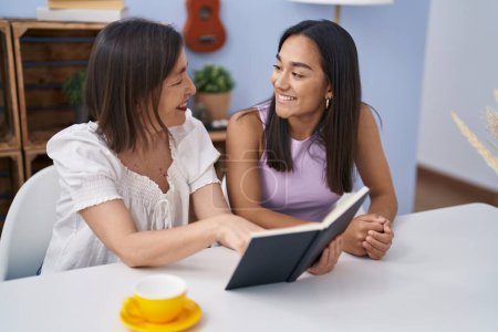 Photo for Two women mother and daughter drinking coffee reading book at home - Royalty Free Image