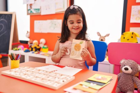 Photo for Adorable hispanic girl playing with vocabulary puzzle game sitting on table at kindergarten - Royalty Free Image