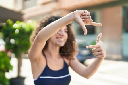 Foto de Joven hermosa mujer hispana sonriendo confiada haciendo gesto fotográfico con las manos en la calle - Imagen libre de derechos