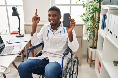 Téléchargez les photos : Un médecin afro-américain assis sur un fauteuil roulant tenant un smartphone surpris par une idée ou une question pointant du doigt avec un visage heureux, numéro un - en image libre de droit