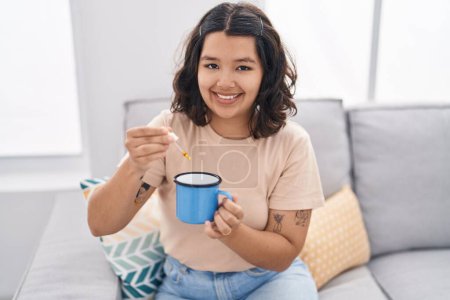 Photo for Young woman smiling confident pouring medication on coffee at home - Royalty Free Image