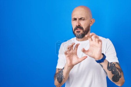Téléchargez les photos : Homme hispanique avec des tatouages debout sur fond bleu expression dégoûtée, mécontent et effrayé faire visage dégoût parce que réaction d'aversion. - en image libre de droit