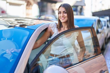 Foto de Joven hermosa mujer hispana sonriendo confiado abriendo la puerta del coche en la calle - Imagen libre de derechos