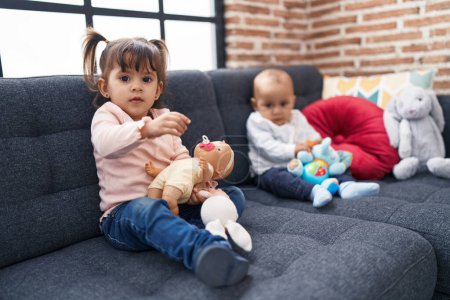Photo for Adorable boy and girl sitting on sofa playing with baby doll at home - Royalty Free Image