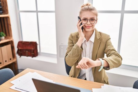 Young blonde woman business worker talking on smartphone looking watch at office Poster 651721838