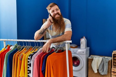 Photo for Young redhead man smiling confident talking on the smartphone at laundry room - Royalty Free Image