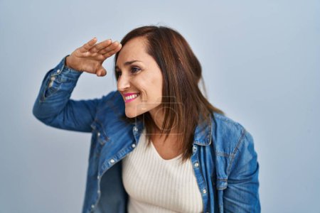 Photo for Middle age brunette woman wearing casual denim jacket over isolated background very happy and smiling looking far away with hand over head. searching concept. - Royalty Free Image