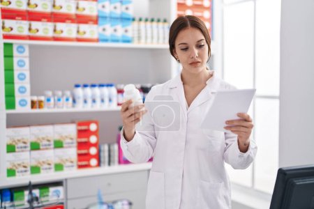 Téléchargez les photos : Young woman pharmacist reading prescription holding pills at pharmacy - en image libre de droit