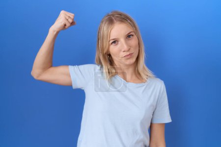 Téléchargez les photos : Jeune femme caucasienne portant casual bleu t-shirt forte personne montrant muscle du bras, confiant et fier de pouvoir - en image libre de droit