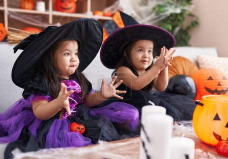 Foto de Adorables chicas gemelas que tienen fiesta de halloween aplaudiendo las manos en casa - Imagen libre de derechos