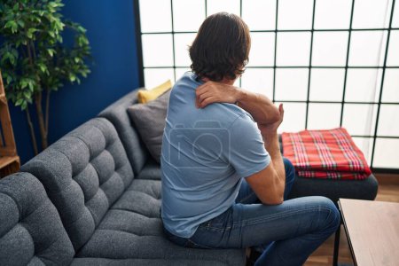 Foto de Hombre de mediana edad que sufre de dolor de espalda sentado en el sofá en casa - Imagen libre de derechos