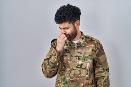 Téléchargez les photos : Un Arabe portant l'uniforme de camouflage de l'armée sentant quelque chose de puant et dégoûtant, une odeur intolérable, retenant son souffle avec les doigts sur le nez. mauvaise odeur - en image libre de droit