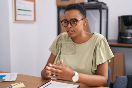 Photo for African american woman business worker sitting on table speaking at office - Royalty Free Image