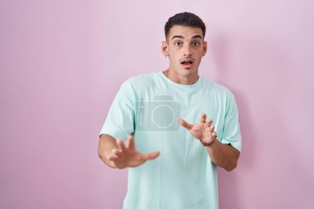 Photo for Handsome hispanic man standing over pink background afraid and terrified with fear expression stop gesture with hands, shouting in shock. panic concept. - Royalty Free Image