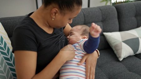 Téléchargez les photos : Mère et son fils assis sur le canapé allaitant bébé à la maison - en image libre de droit