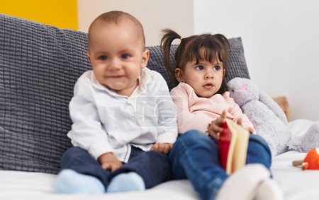 Téléchargez les photos : Adorable livre de lecture garçon et fille assis sur le lit à la maison - en image libre de droit