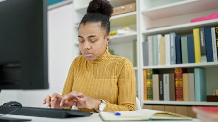 Téléchargez les photos : Jeune étudiante afro-américaine utilisant un ordinateur étudiant à la bibliothèque - en image libre de droit