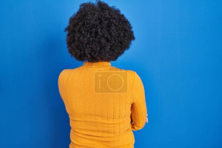 Photo for Black woman with curly hair standing over blue background standing backwards looking away with crossed arms - Royalty Free Image