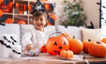 Photo for Adorable hispanic girl wearing halloween costume holding candies of bowl at home - Royalty Free Image
