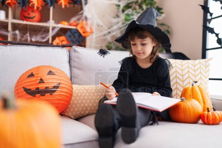 Téléchargez les photos : Adorable hispanique fille dessin sur ordinateur portable ayant fête d'Halloween à la maison - en image libre de droit