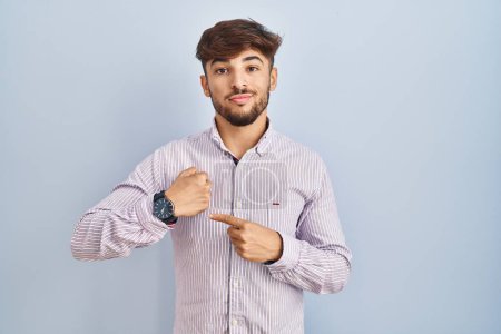 Photo for Arab man with beard standing over blue background in hurry pointing to watch time, impatience, looking at the camera with relaxed expression - Royalty Free Image