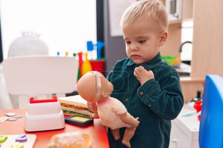 Photo for Adorable caucasian boy standing with relaxed expression playing with baby doll at kindergarten - Royalty Free Image