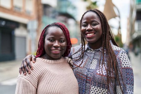 Foto de Afro-americanas amigas sonriendo confiadas abrazándose en la calle - Imagen libre de derechos