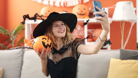 Téléchargez les photos : Jeune femme blonde tenant panier de citrouille halloween faire selfie par smartphone à la maison - en image libre de droit