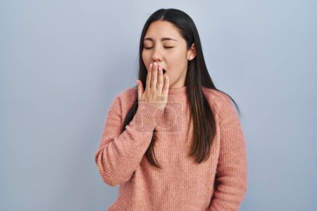 Photo for Young latin woman standing over blue background bored yawning tired covering mouth with hand. restless and sleepiness. - Royalty Free Image