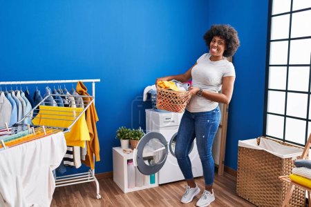 Foto de African american woman smiling confident holding basket with clothes at laundry room - Imagen libre de derechos