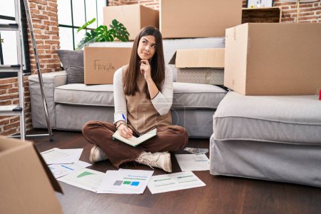 Photo for Young brunette woman moving to a new home doing finances serious face thinking about question with hand on chin, thoughtful about confusing idea - Royalty Free Image