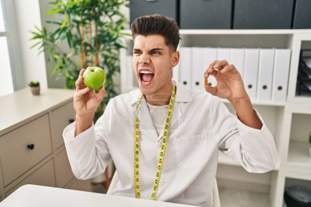 Photo for Young hispanic doctor man holding pills for fat loss angry and mad screaming frustrated and furious, shouting with anger. rage and aggressive concept. - Royalty Free Image