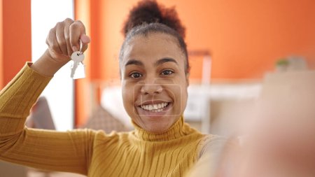 Téléchargez les photos : Jeune femme afro-américaine souriante confiante tenant la clé faisant appel vidéo à la nouvelle maison - en image libre de droit