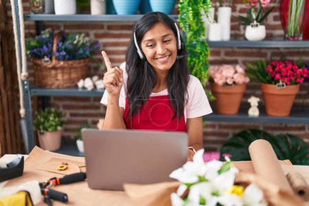 Photo for Young hispanic woman working at florist shop doing video call smiling happy pointing with hand and finger to the side - Royalty Free Image