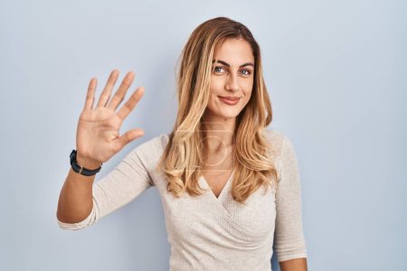 Photo for Young blonde woman standing over isolated background showing and pointing up with fingers number five while smiling confident and happy. - Royalty Free Image
