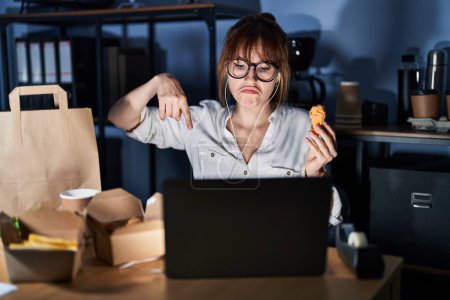 Photo for Young beautiful woman working using computer laptop and eating delivery food pointing down looking sad and upset, indicating direction with fingers, unhappy and depressed. - Royalty Free Image