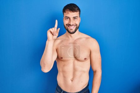 Photo for Handsome hispanic man standing shirtless showing and pointing up with finger number one while smiling confident and happy. - Royalty Free Image