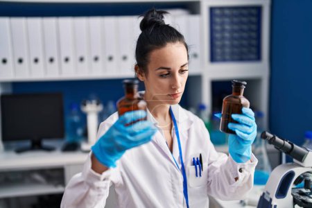 Foto de Joven mujer caucásica científica sosteniendo botellas en laboratorio - Imagen libre de derechos