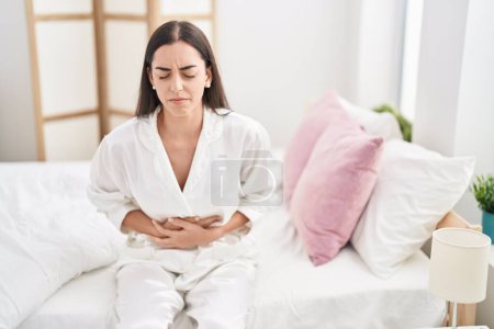 Photo for Young hispanic woman suffering for menstrual pain sitting on bed at bedroom - Royalty Free Image