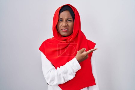 Téléchargez les photos : Jeune femme arabe portant l'écharpe traditionnelle islamique hijab pointant de côté inquiet et nerveux avec index, expression inquiète et surprise - en image libre de droit