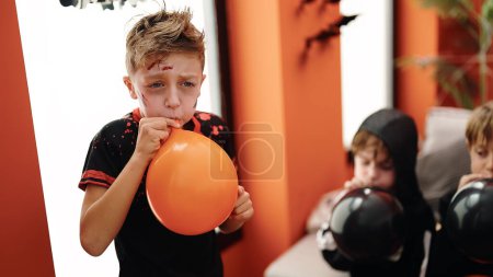 Foto de Adorable chicos usando halloween traje soplando globo en casa - Imagen libre de derechos