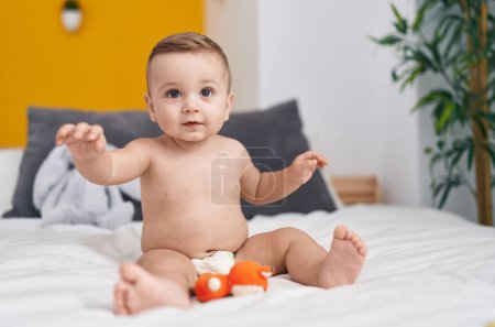 Téléchargez les photos : Adorable bébé caucasien jouant avec jouet assis sur le lit dans la chambre - en image libre de droit
