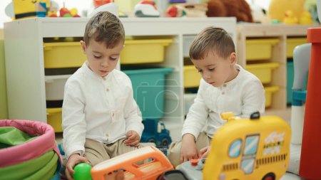 Téléchargez les photos : Adorables garçons assis sur le sol jouant avec des jouets de voiture à la maternelle - en image libre de droit